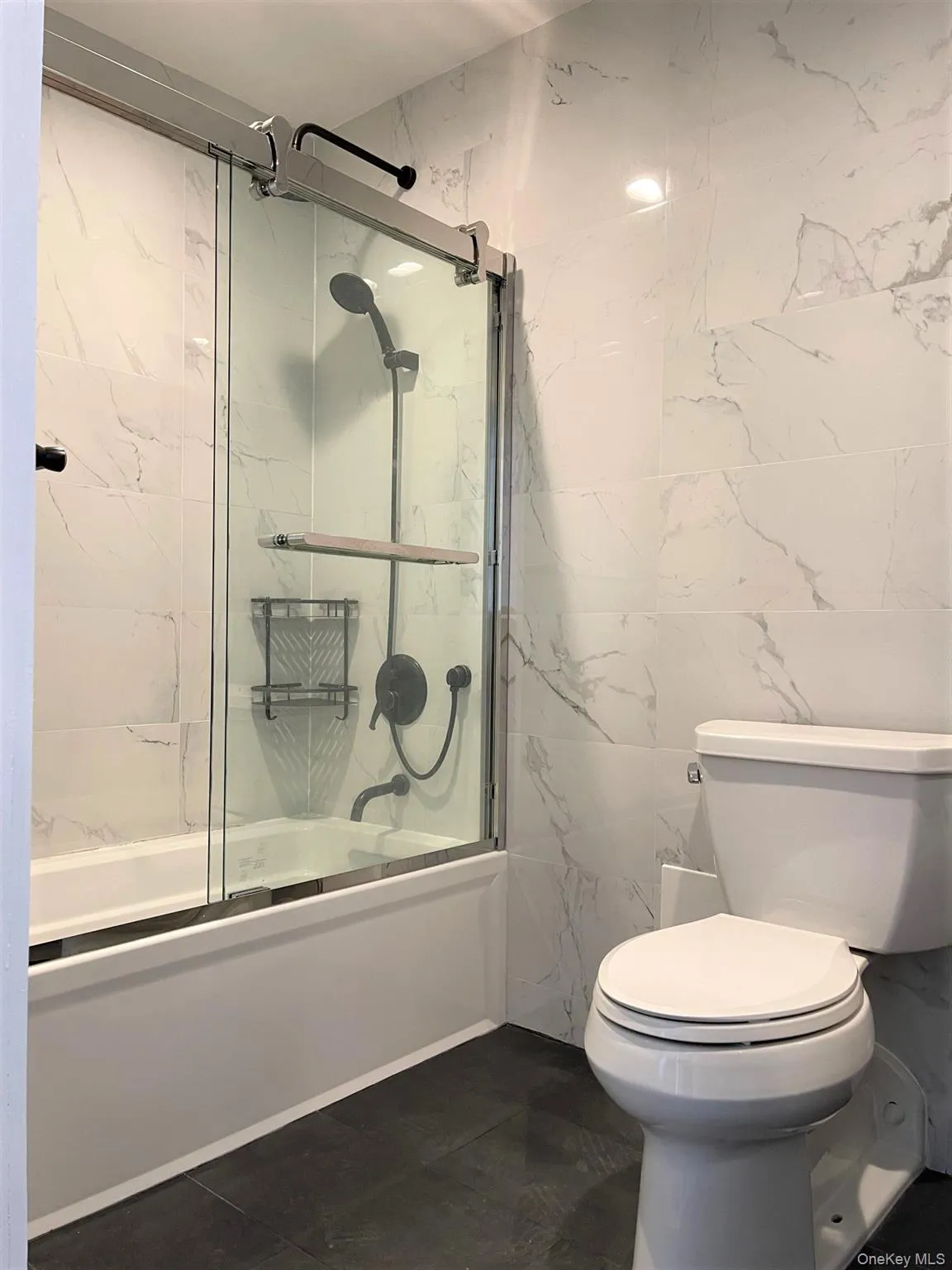 Full bath with tile walls, shower / bath combination with glass door, and dark tile patterned flooring Full bath with tile walls, shower / bath combination with glass door, and dark tile patterned flooring