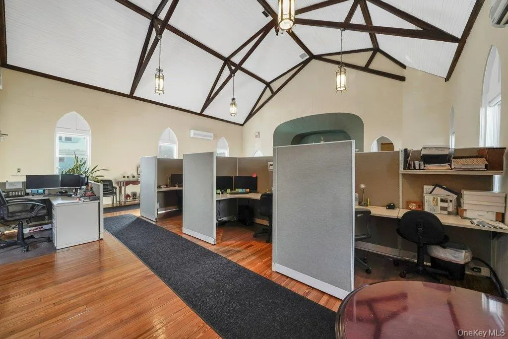 Office area with high vaulted ceiling, wood finished floors, beamed ceiling, built in study area, and a wall unit AC Office area with high vaulted ceiling, wood finished floors, beamed ceiling, built in study area, and a wall unit AC