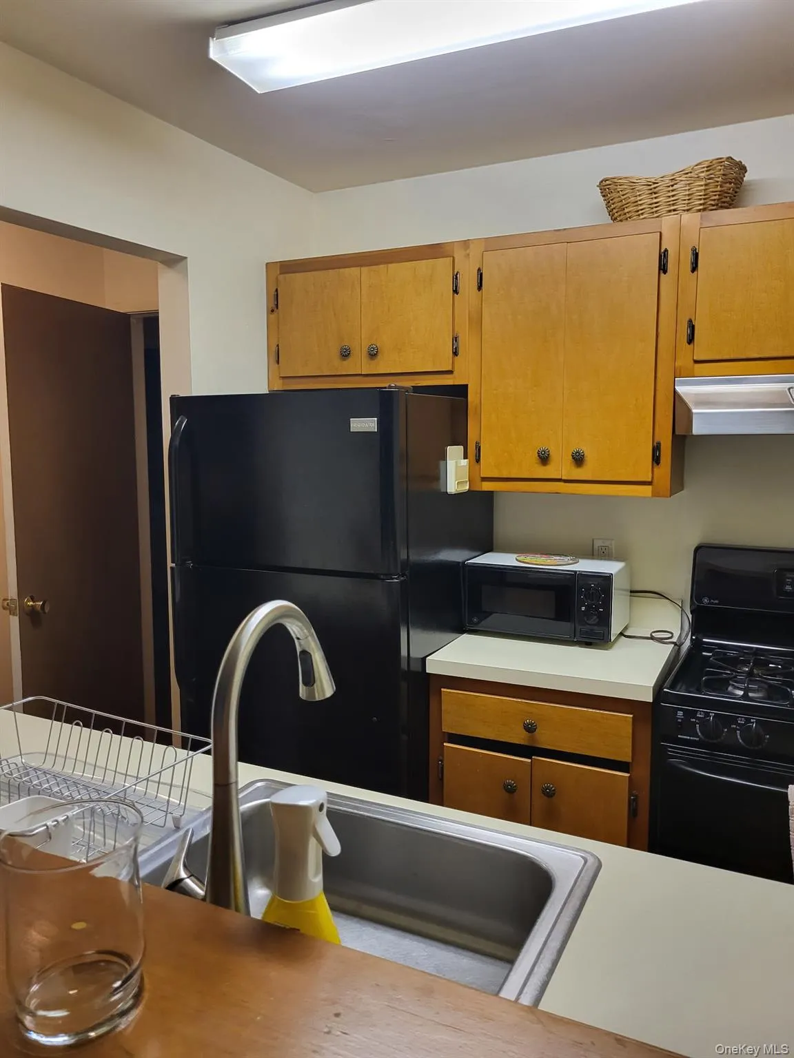 Kitchen with light countertops, black appliances, brown cabinets, and ventilation hood Kitchen with light countertops, black appliances, brown cabinets, and ventilation hood