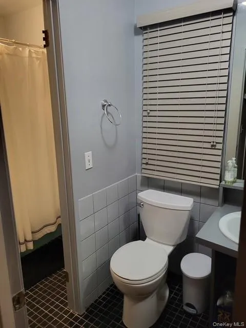 Full bath featuring dark tile patterned floors, vanity, a shower with curtain, and tile walls Full bath featuring dark tile patterned floors, vanity, a shower with curtain, and tile walls