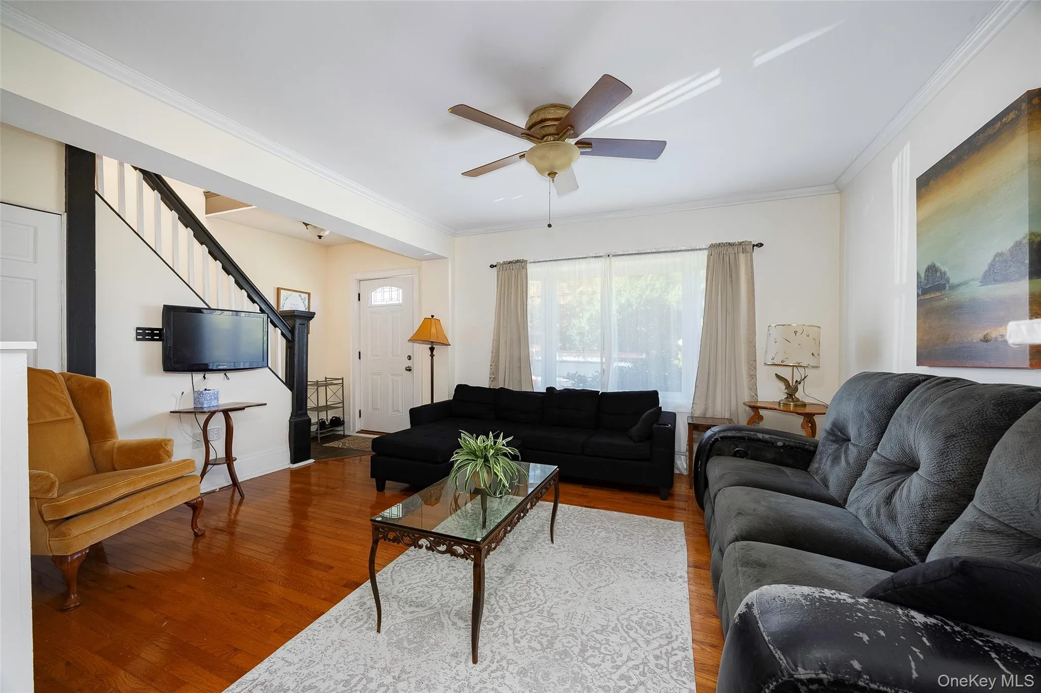 Living area featuring wood finished floors, ornamental molding, stairway, and a ceiling fan Living area featuring wood finished floors, ornamental molding, stairway, and a ceiling fan