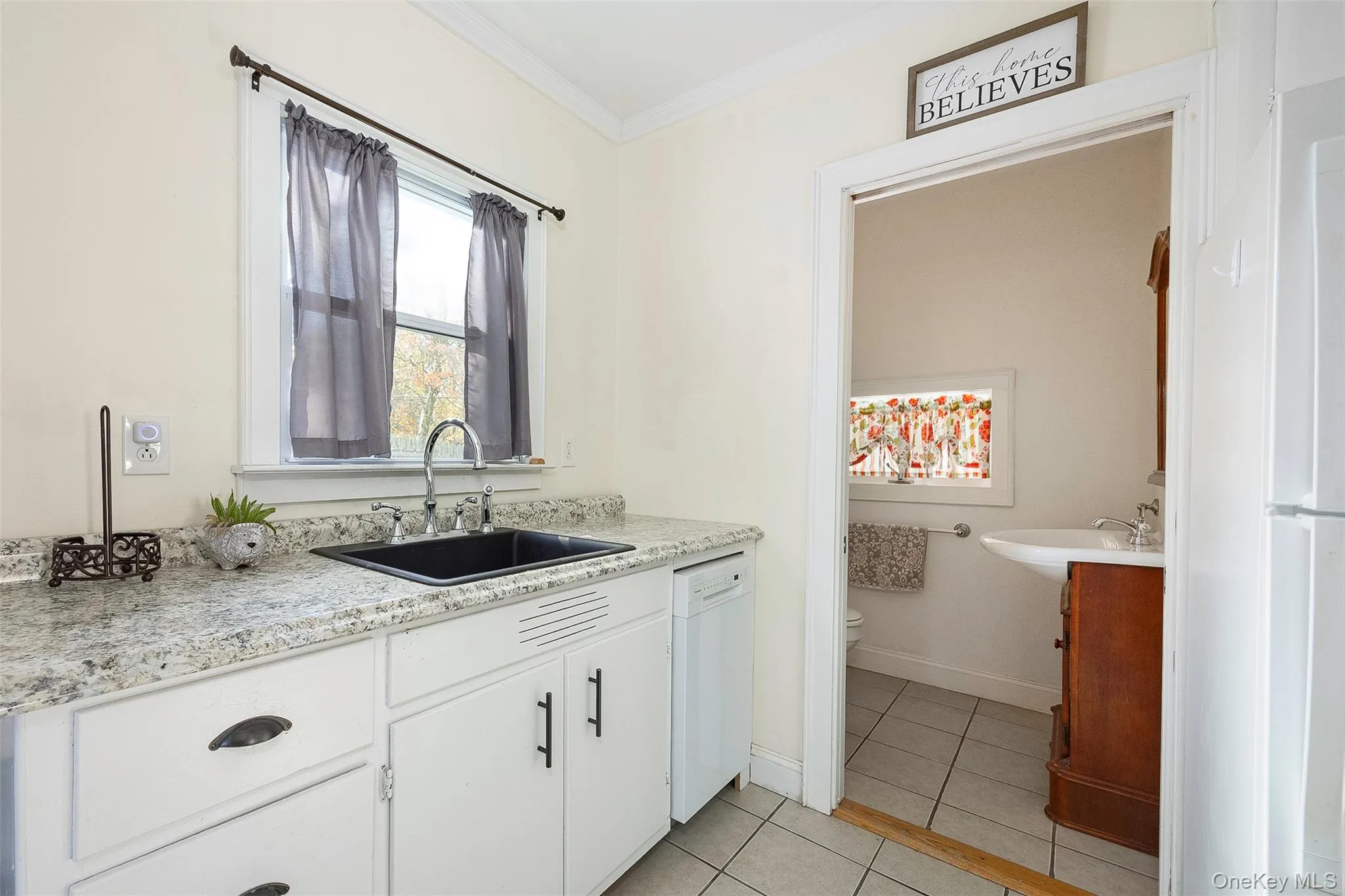 Kitchen with white cabinetry, white appliances, light tile patterned flooring, ornamental molding, and light stone countertops Kitchen with white cabinetry, white appliances, light tile patterned flooring, ornamental molding, and light stone countertops