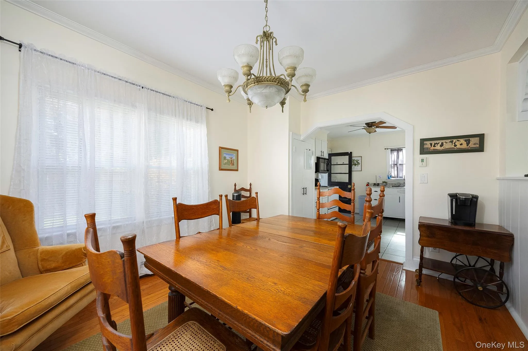 Dining area featuring crown molding, dark wood-style flooring, a chandelier, a ceiling fan, and arched walkways Dining area featuring crown molding, dark wood-style flooring, a chandelier, a ceiling fan, and arched walkways