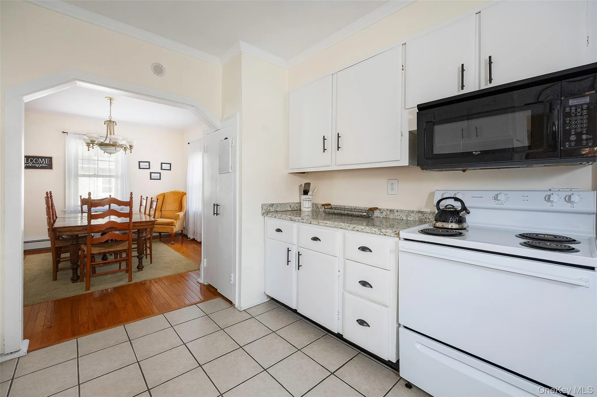 Kitchen featuring electric range, black microwave, white cabinets, ornamental molding, and a chandelier Kitchen featuring electric range, black microwave, white cabinets, ornamental molding, and a chandelier