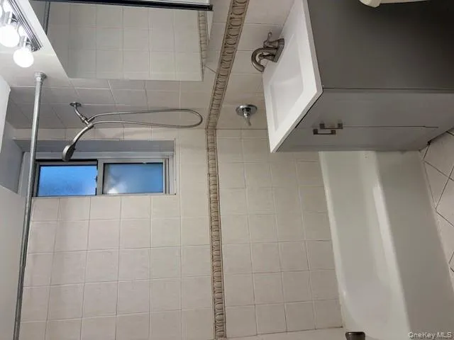 Bathroom with shower / bathtub combination, vanity, light tile patterned flooring, and tile walls Bathroom with shower / bathtub combination, vanity, light tile patterned flooring, and tile walls