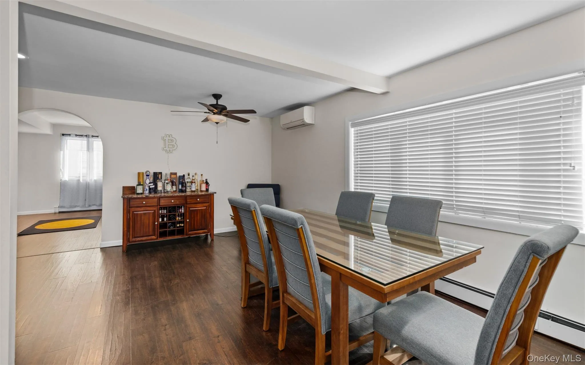 Dining area featuring beamed ceiling, dark wood-style flooring, arched walkways, a baseboard heating unit, and ceiling fan Dining area featuring beamed ceiling, dark wood-style flooring, arched walkways, a baseboard heating unit, and ceiling fan
