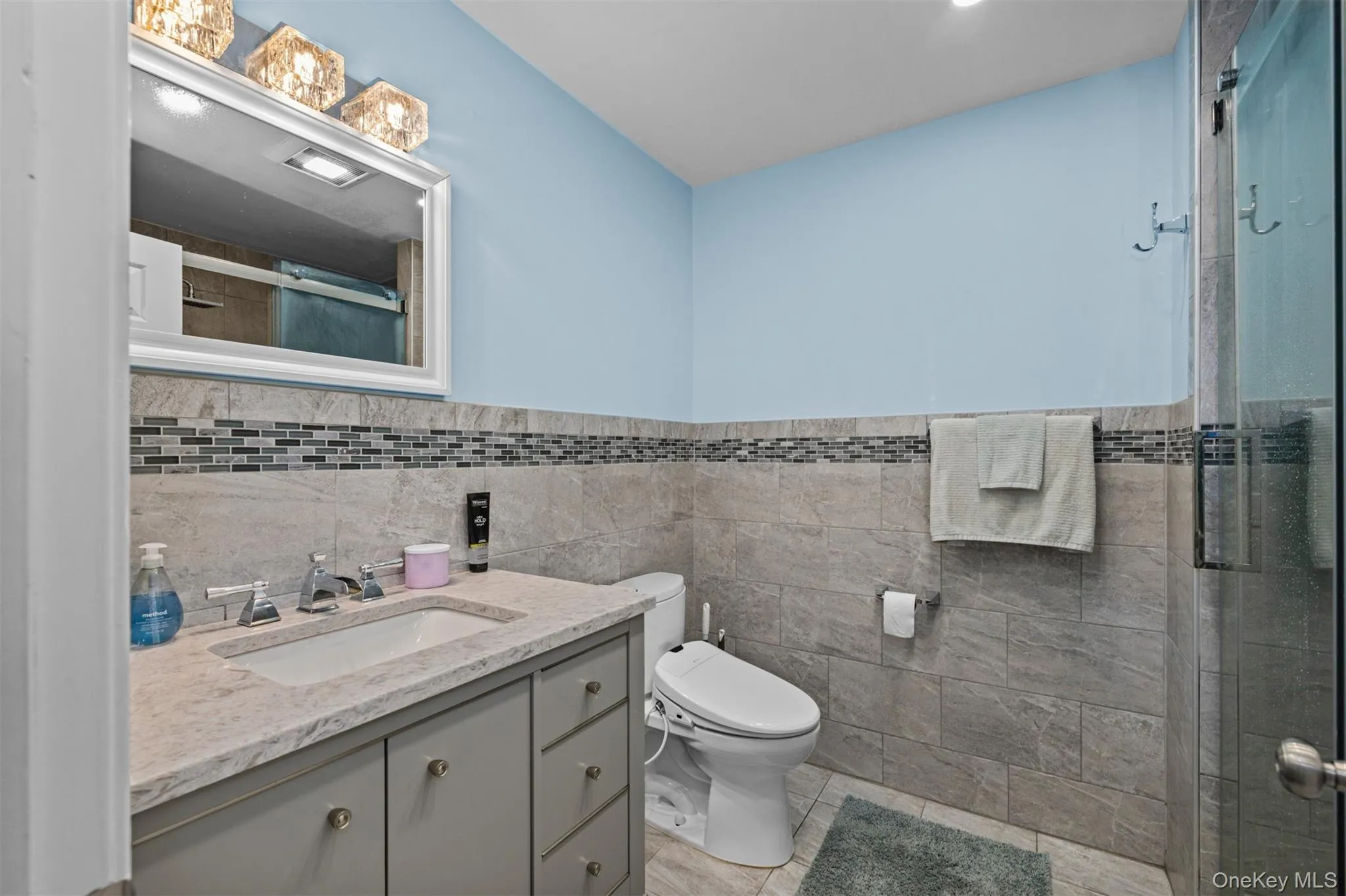 Full bath with vanity, tile walls, a wainscoted wall, and a stall shower Full bath with vanity, tile walls, a wainscoted wall, and a stall shower