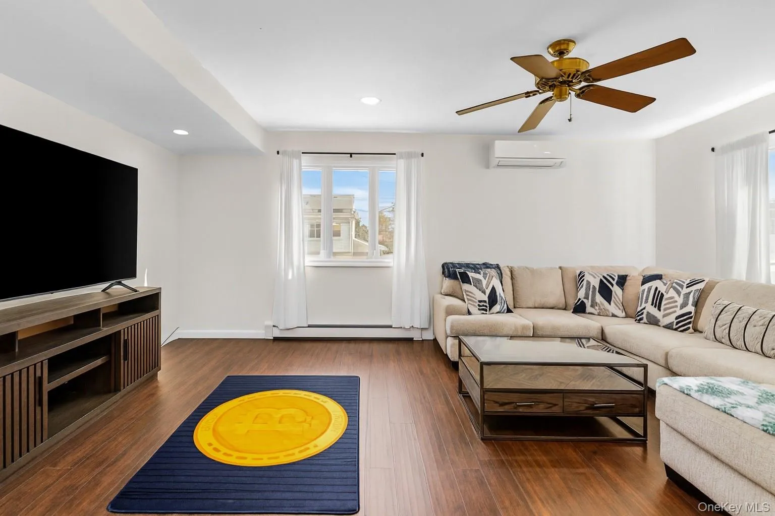 Living area with dark wood-type flooring, recessed lighting, a ceiling fan, a wall mounted air conditioner, and baseboard heating Living area with dark wood-type flooring, recessed lighting, a ceiling fan, a wall mounted air conditioner, and baseboard heating