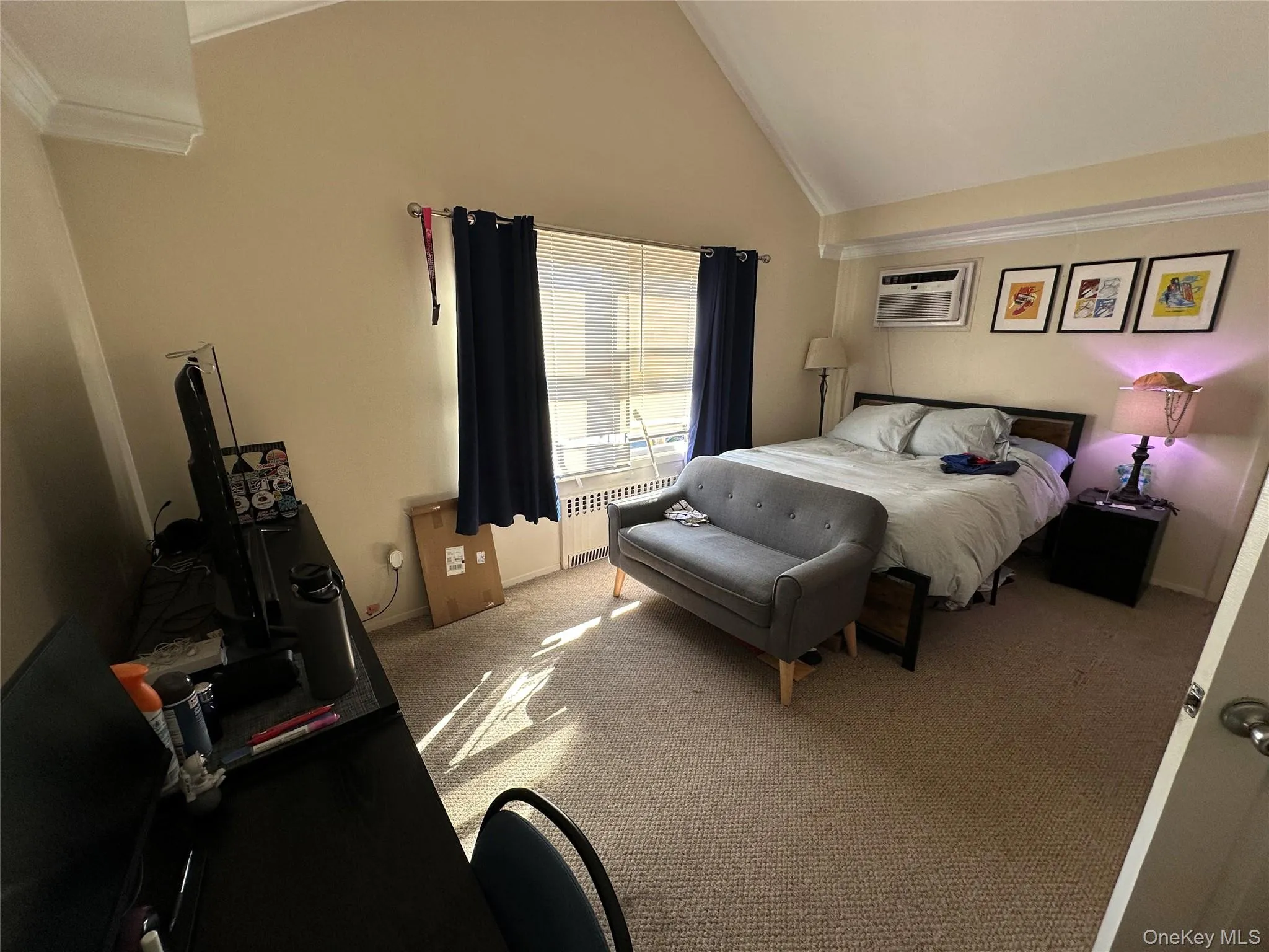 Carpeted bedroom with radiator heating unit, lofted ceiling, and an AC wall unit Carpeted bedroom with radiator heating unit, lofted ceiling, and an AC wall unit