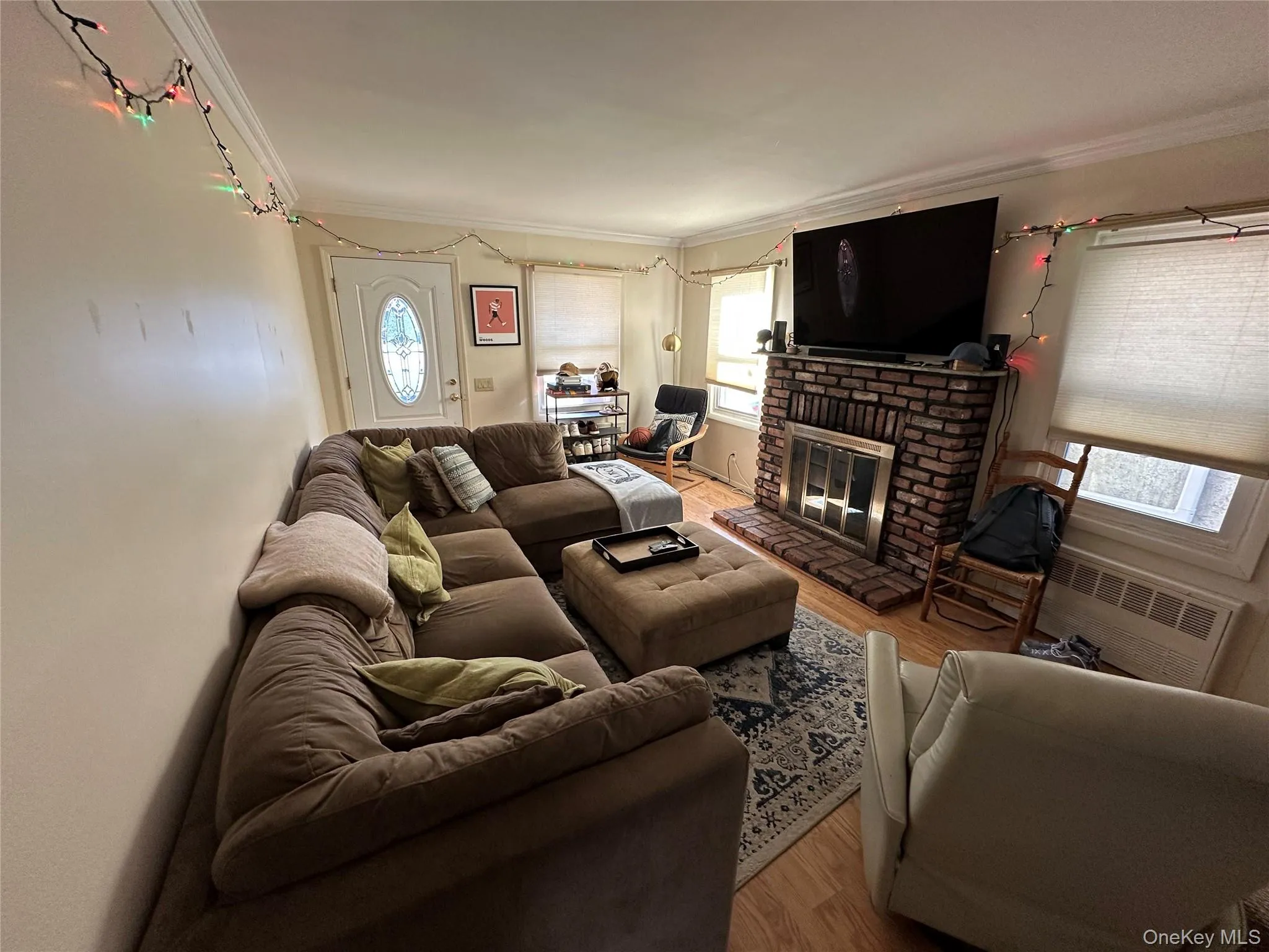Living room featuring radiator heating unit, wood finished floors, a fireplace, and crown molding Living room featuring radiator heating unit, wood finished floors, a fireplace, and crown molding