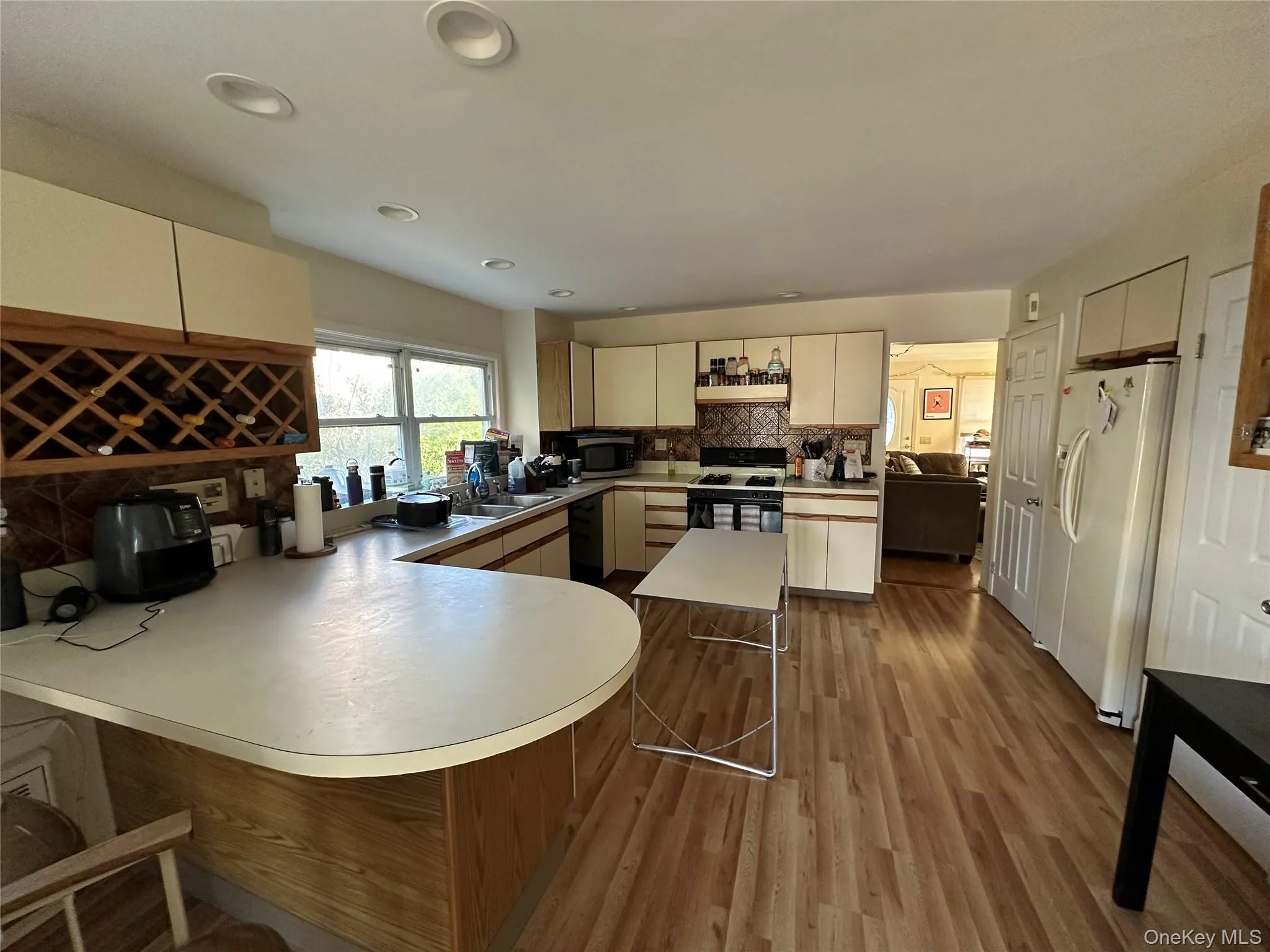 Kitchen with a breakfast bar area, tasteful backsplash, dark wood-style flooring, white fridge with ice dispenser, and a peninsula Kitchen with a breakfast bar area, tasteful backsplash, dark wood-style flooring, white fridge with ice dispenser, and a peninsula