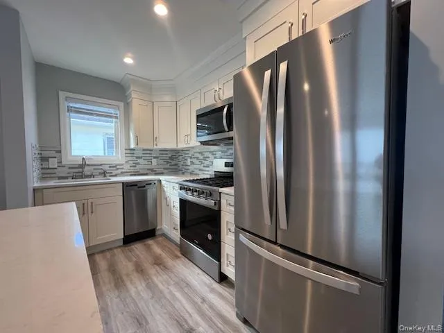 Kitchen with appliances with stainless steel finishes, light wood-type flooring, backsplash, white cabinets, and recessed lighting Kitchen with appliances with stainless steel finishes, light wood-type flooring, backsplash, white cabinets, and recessed lighting