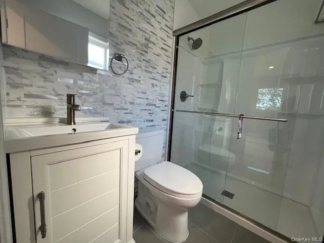Full bath featuring a shower stall, vanity, tile patterned floors, and tile walls Full bath featuring a shower stall, vanity, tile patterned floors, and tile walls