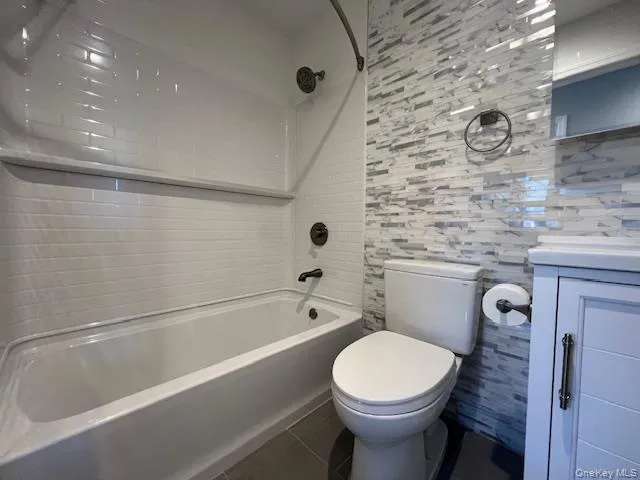 Bathroom featuring shower combination, vanity, dark tile patterned floors, and tile walls Bathroom featuring shower combination, vanity, dark tile patterned floors, and tile walls