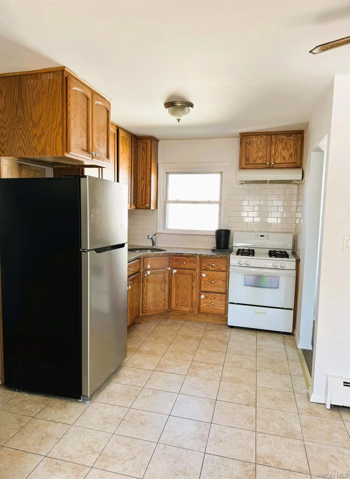 Kitchen featuring freestanding refrigerator, white gas range, brown cabinets, and backsplash Kitchen featuring freestanding refrigerator, white gas range, brown cabinets, and backsplash