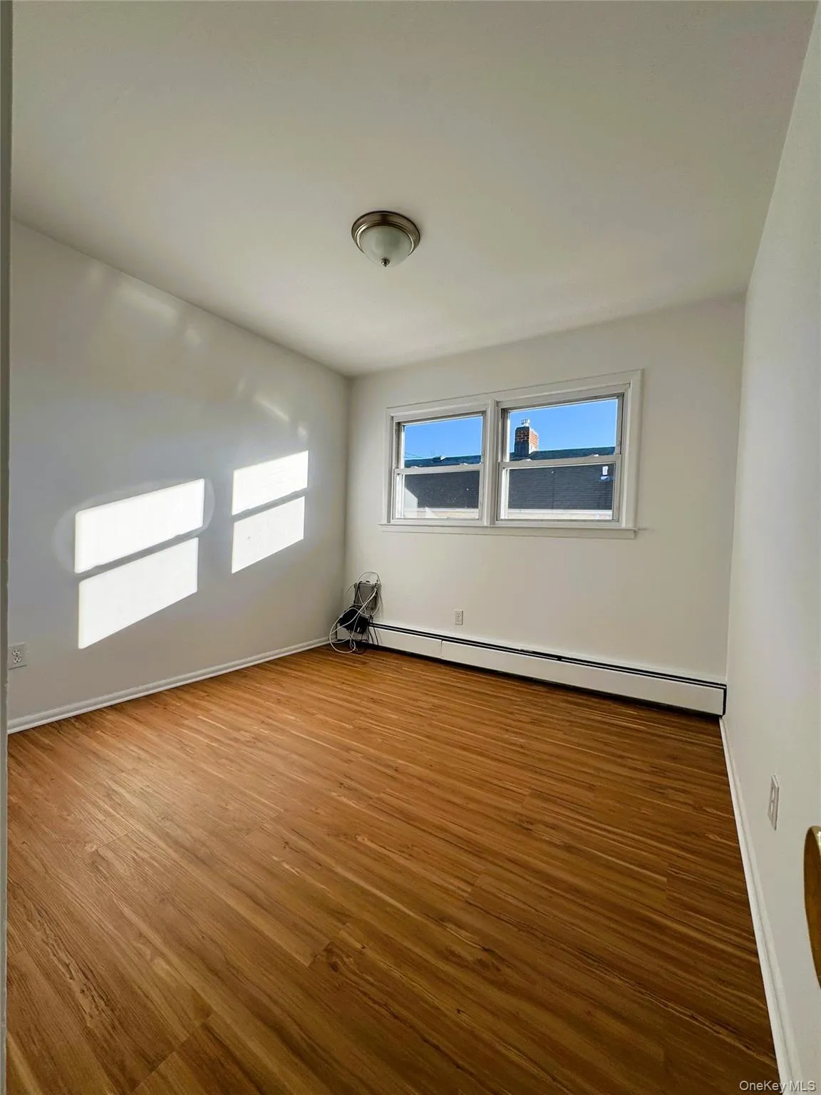 Spare room with wood finished floors, a baseboard radiator, and plenty of natural light Spare room with wood finished floors, a baseboard radiator, and plenty of natural light