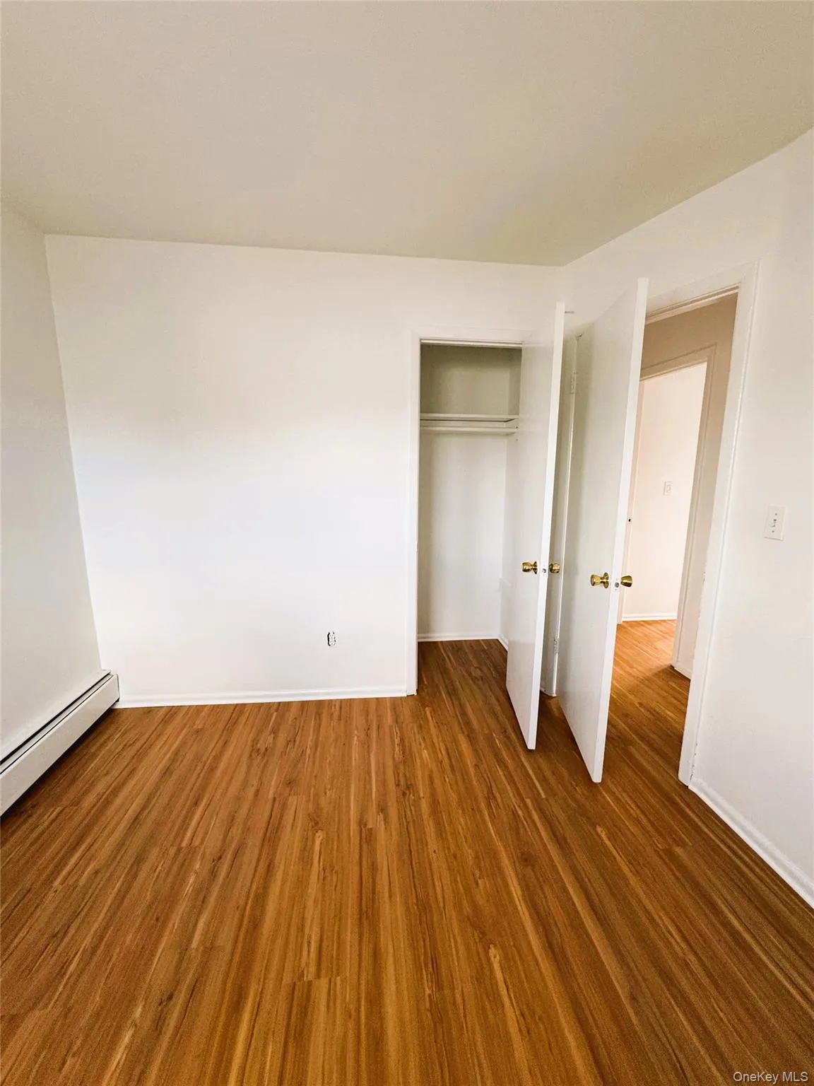 Unfurnished bedroom featuring a baseboard heating unit, dark wood finished floors, and a closet Unfurnished bedroom featuring a baseboard heating unit, dark wood finished floors, and a closet