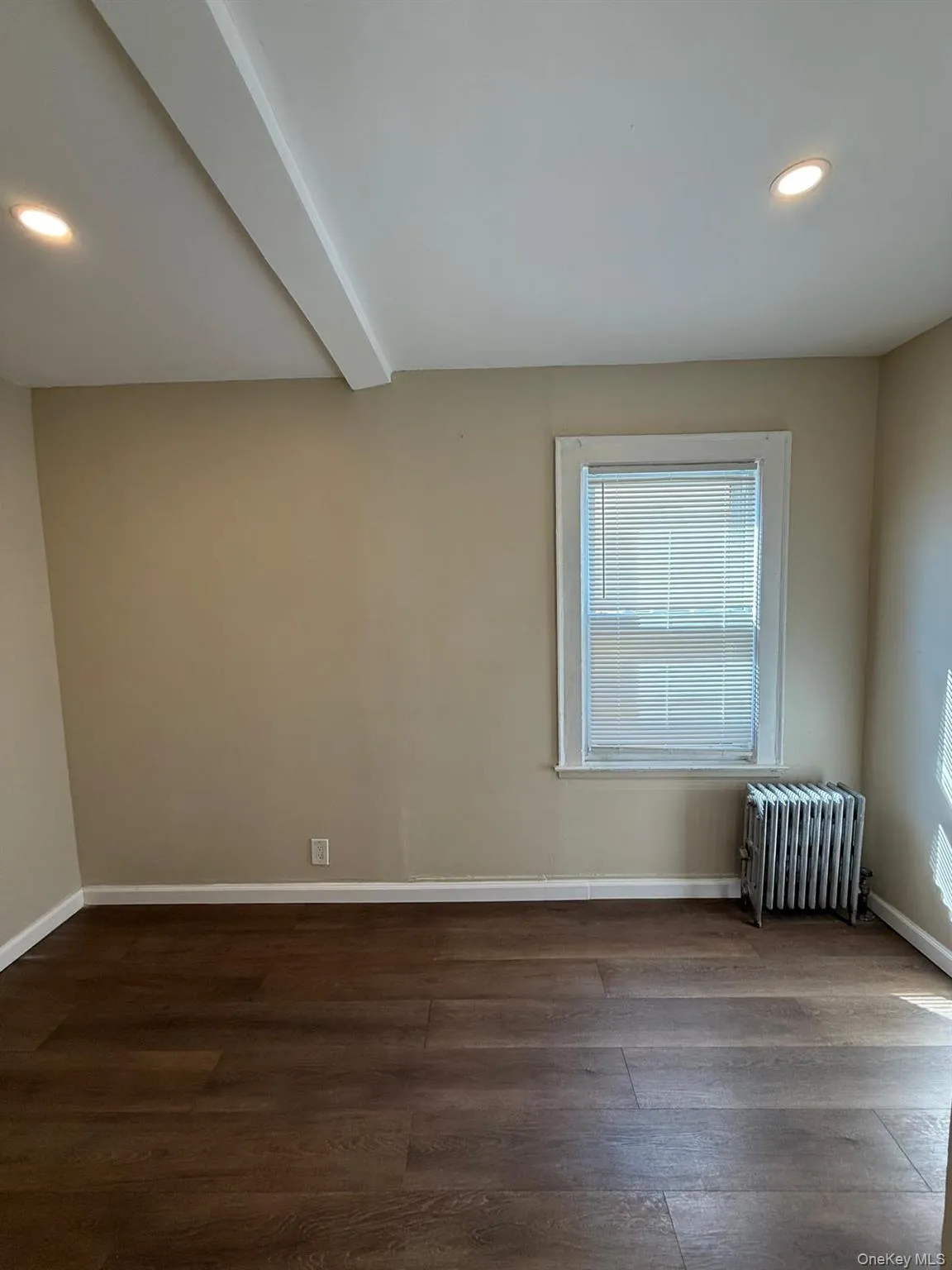 Empty room with recessed lighting, beam ceiling, radiator, and dark wood-type flooring Empty room with recessed lighting, beam ceiling, radiator, and dark wood-type flooring