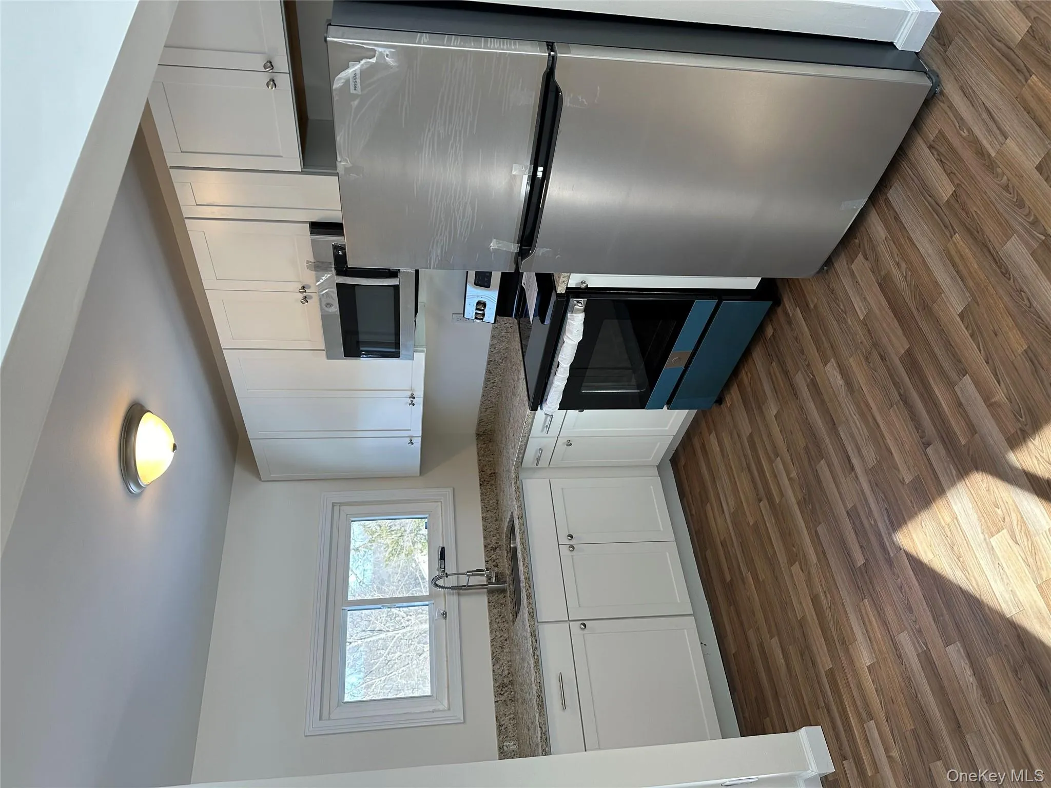 Kitchen with refrigerator, white cabinetry, range with electric stovetop, stainless steel microwave, and dark wood-style flooring Kitchen with refrigerator, white cabinetry, range with electric stovetop, stainless steel microwave, and dark wood-style flooring