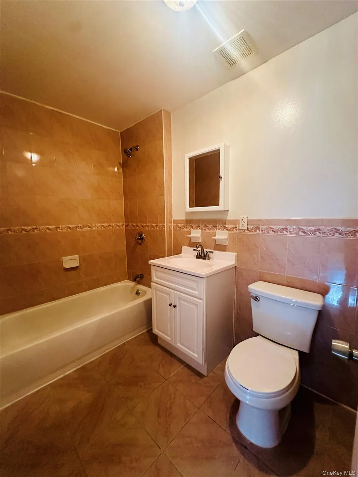 Bathroom featuring tile walls, vanity, shower combination, wainscoting, and light tile patterned floors Bathroom featuring tile walls, vanity, shower combination, wainscoting, and light tile patterned floors