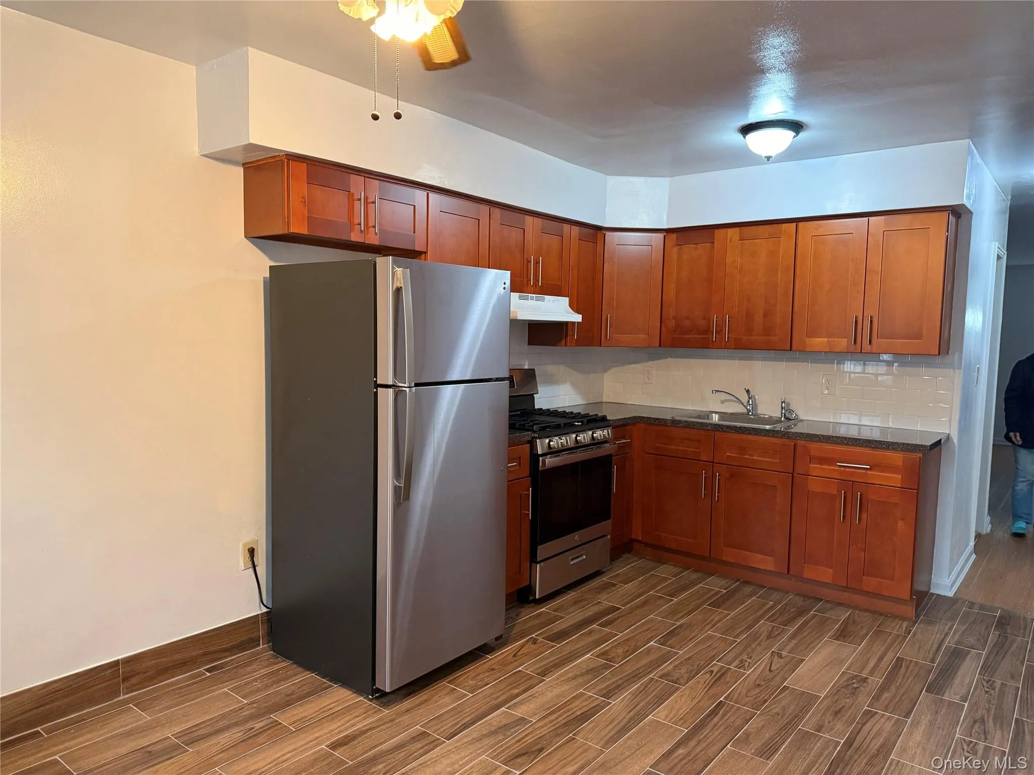 Kitchen featuring appliances with stainless steel finishes, decorative backsplash, wood tiled floors, brown cabinets, and dark stone counters Kitchen featuring appliances with stainless steel finishes, decorative backsplash, wood tiled floors, brown cabinets, and dark stone counters