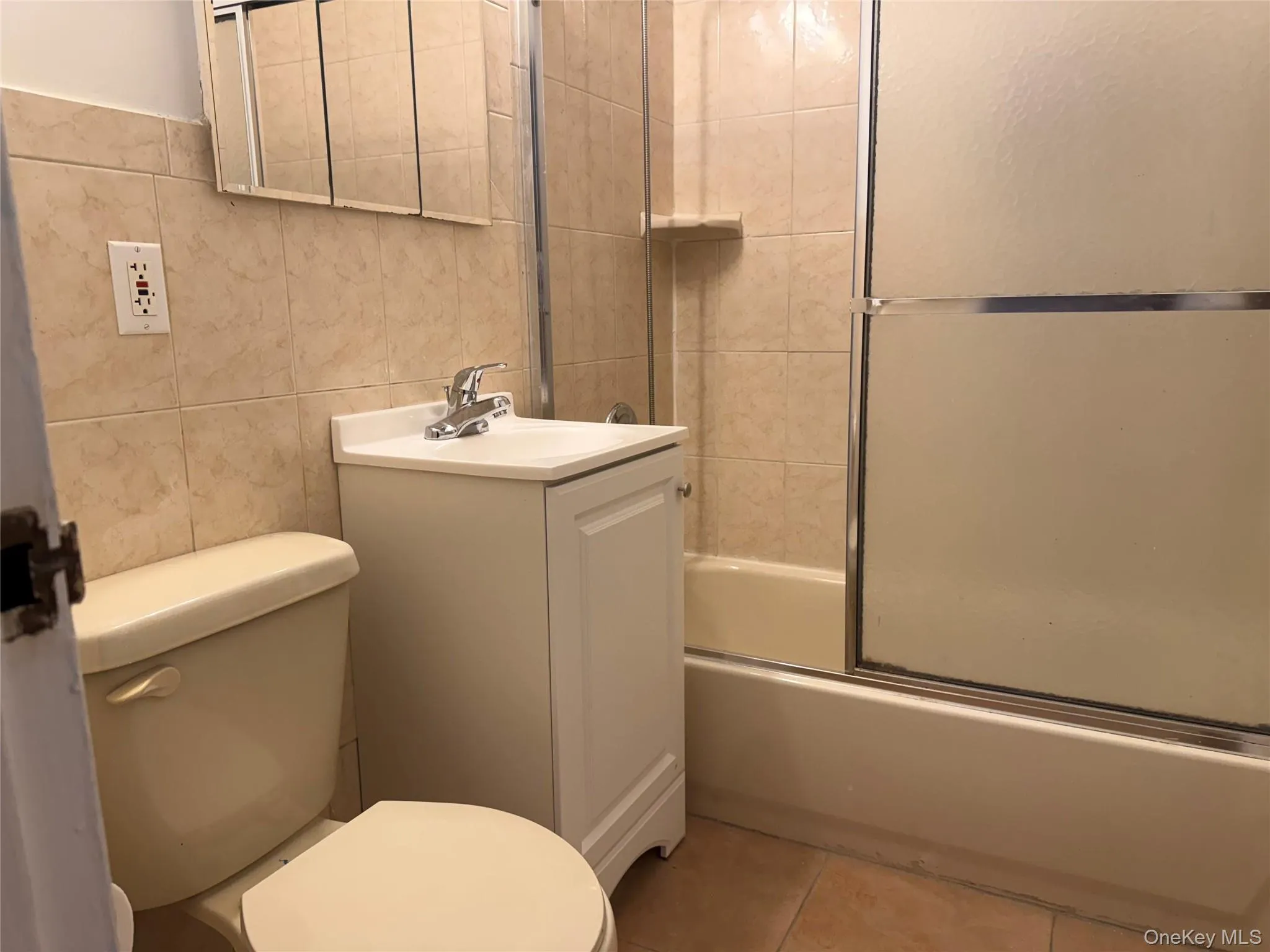 Bathroom featuring tile walls, vanity, combined bath / shower with glass door, and light tile patterned floors Bathroom featuring tile walls, vanity, combined bath / shower with glass door, and light tile patterned floors
