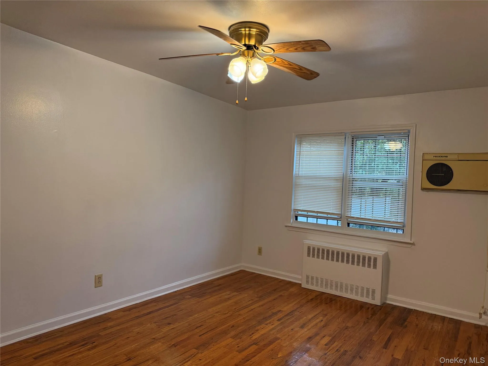Spare room with radiator, dark wood-style flooring, and ceiling fan Spare room with radiator, dark wood-style flooring, and ceiling fan