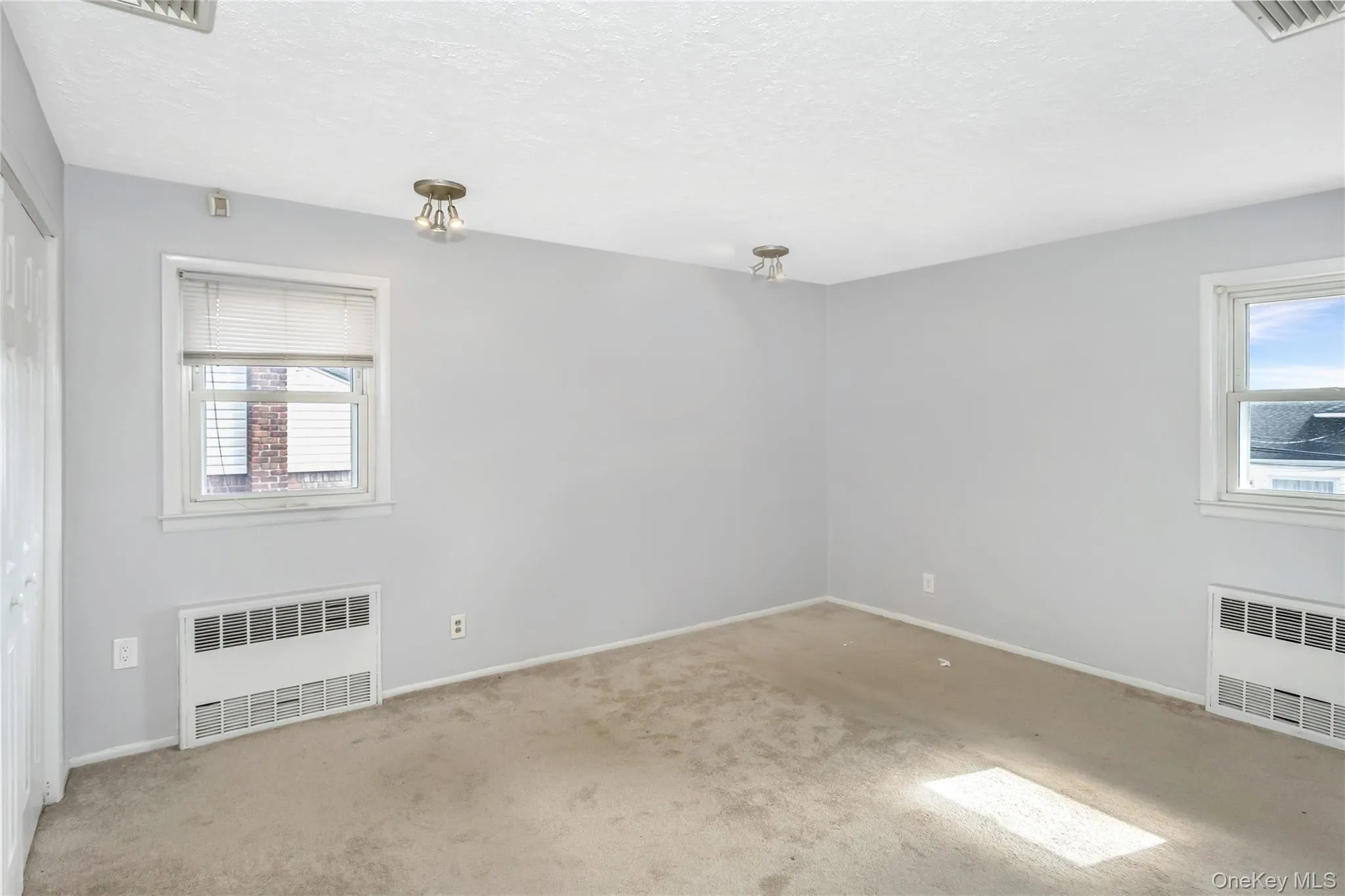 Empty room with radiator heating unit, a textured ceiling, and carpet floors Empty room with radiator heating unit, a textured ceiling, and carpet floors