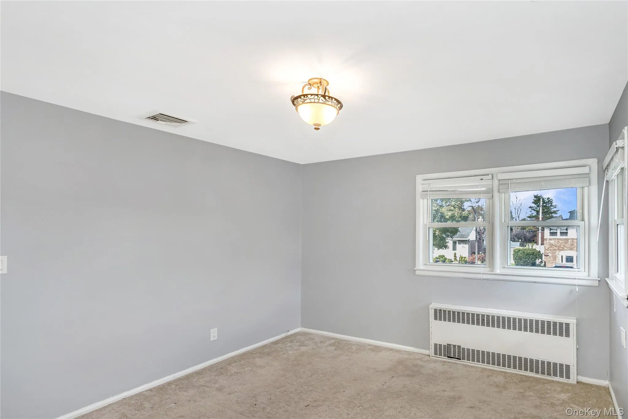 Carpeted empty room featuring radiator heating unit and baseboards Carpeted empty room featuring radiator heating unit and baseboards