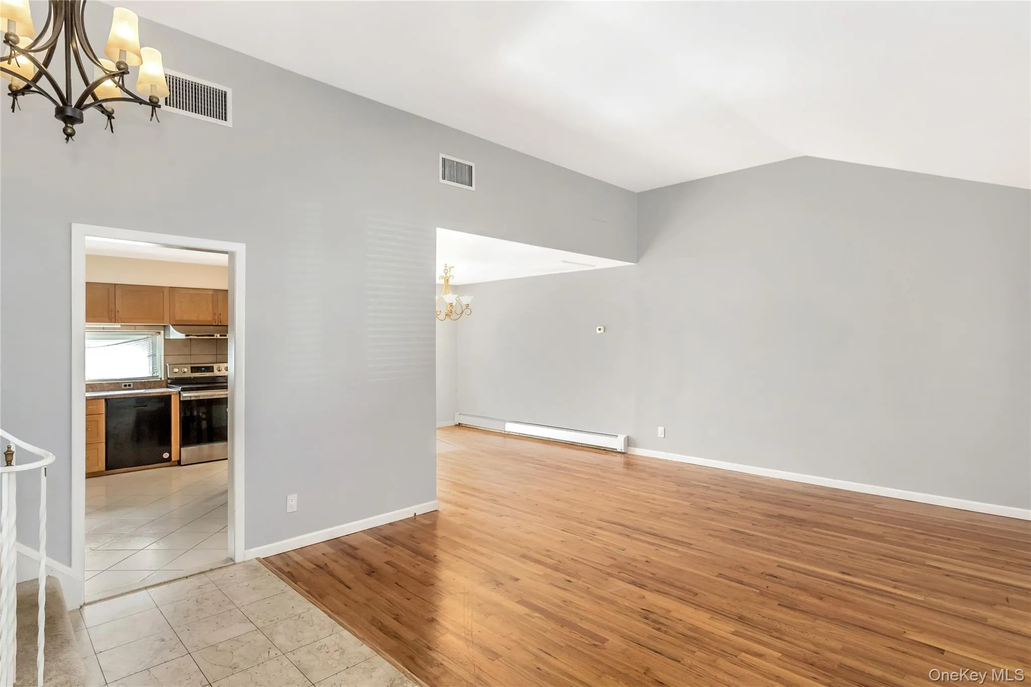 Unfurnished living room with a chandelier, light wood-style floors, lofted ceiling, and baseboard heating Unfurnished living room with a chandelier, light wood-style floors, lofted ceiling, and baseboard heating