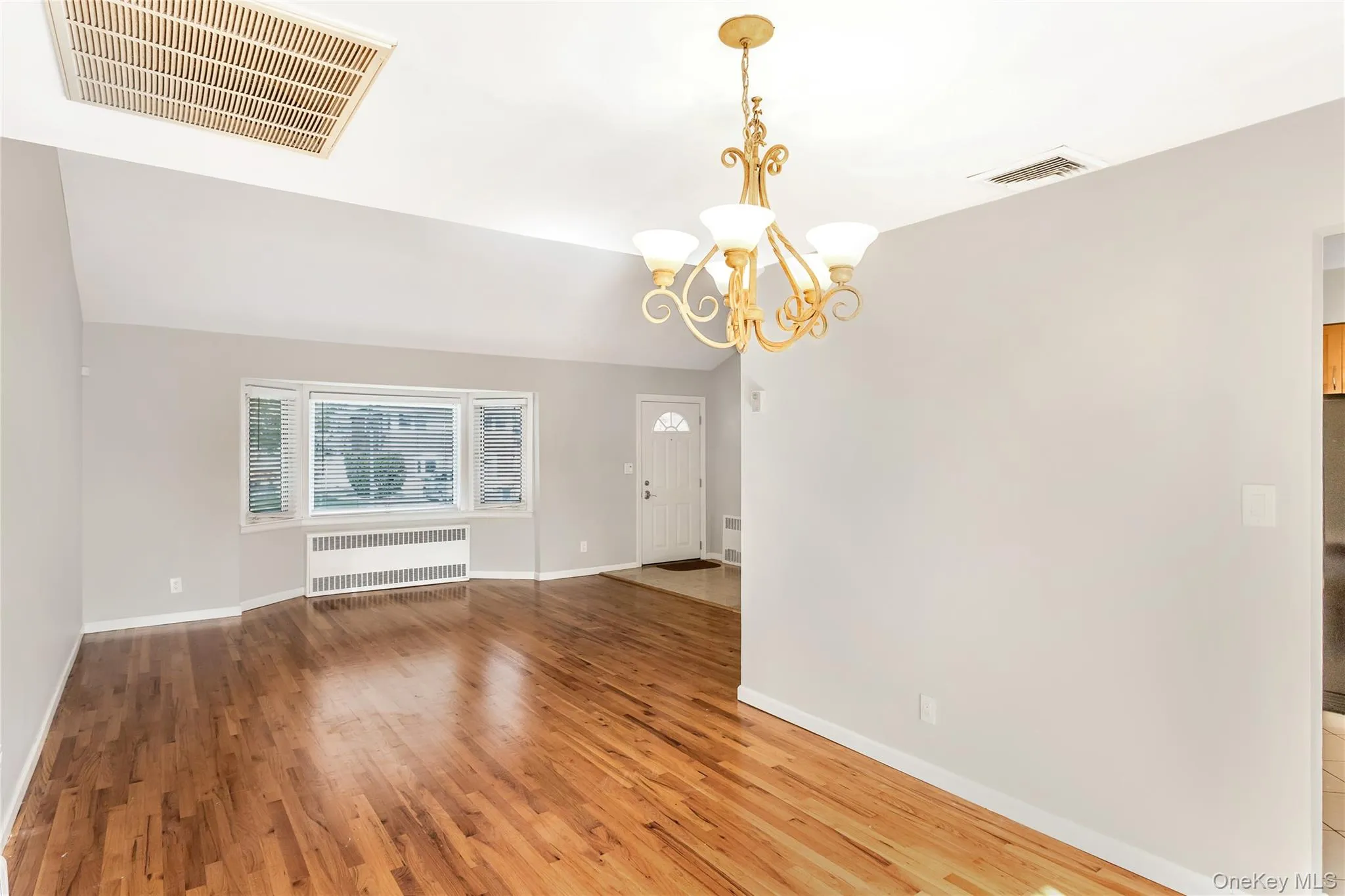 Spare room with wood finished floors, a chandelier, radiator, and vaulted ceiling Spare room with wood finished floors, a chandelier, radiator, and vaulted ceiling
