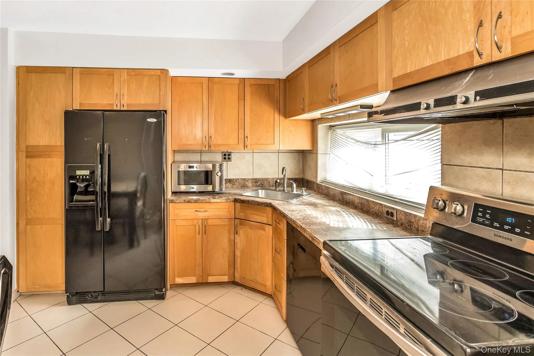 Kitchen featuring black appliances, brown cabinetry, exhaust hood, and light tile patterned floors Kitchen featuring black appliances, brown cabinetry, exhaust hood, and light tile patterned floors