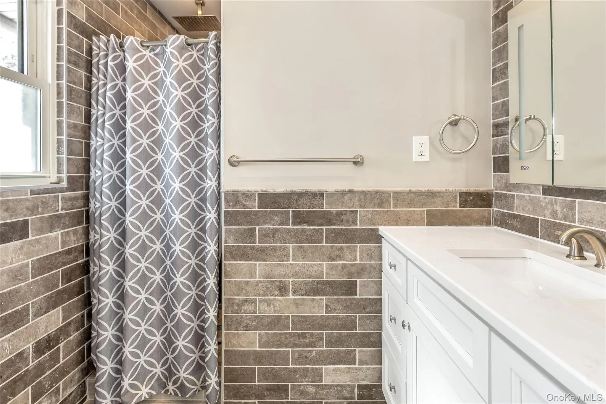 Full bath with vanity, tile walls, a tile shower, and a wainscoted wall Full bath with vanity, tile walls, a tile shower, and a wainscoted wall