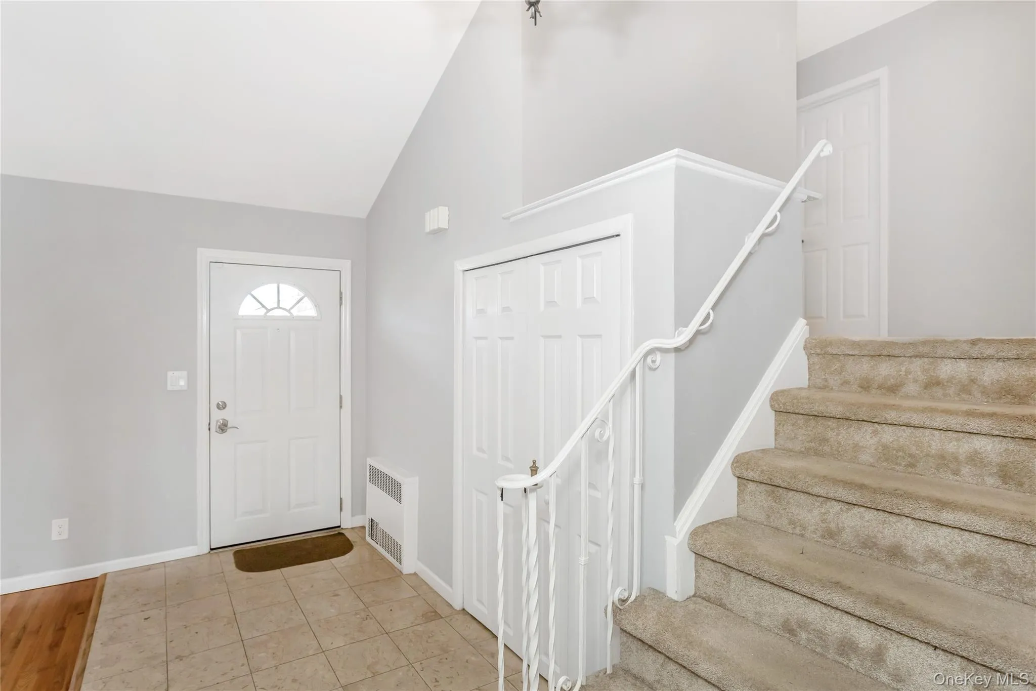 Entryway with light tile patterned floors, lofted ceiling, radiator, and stairs Entryway with light tile patterned floors, lofted ceiling, radiator, and stairs