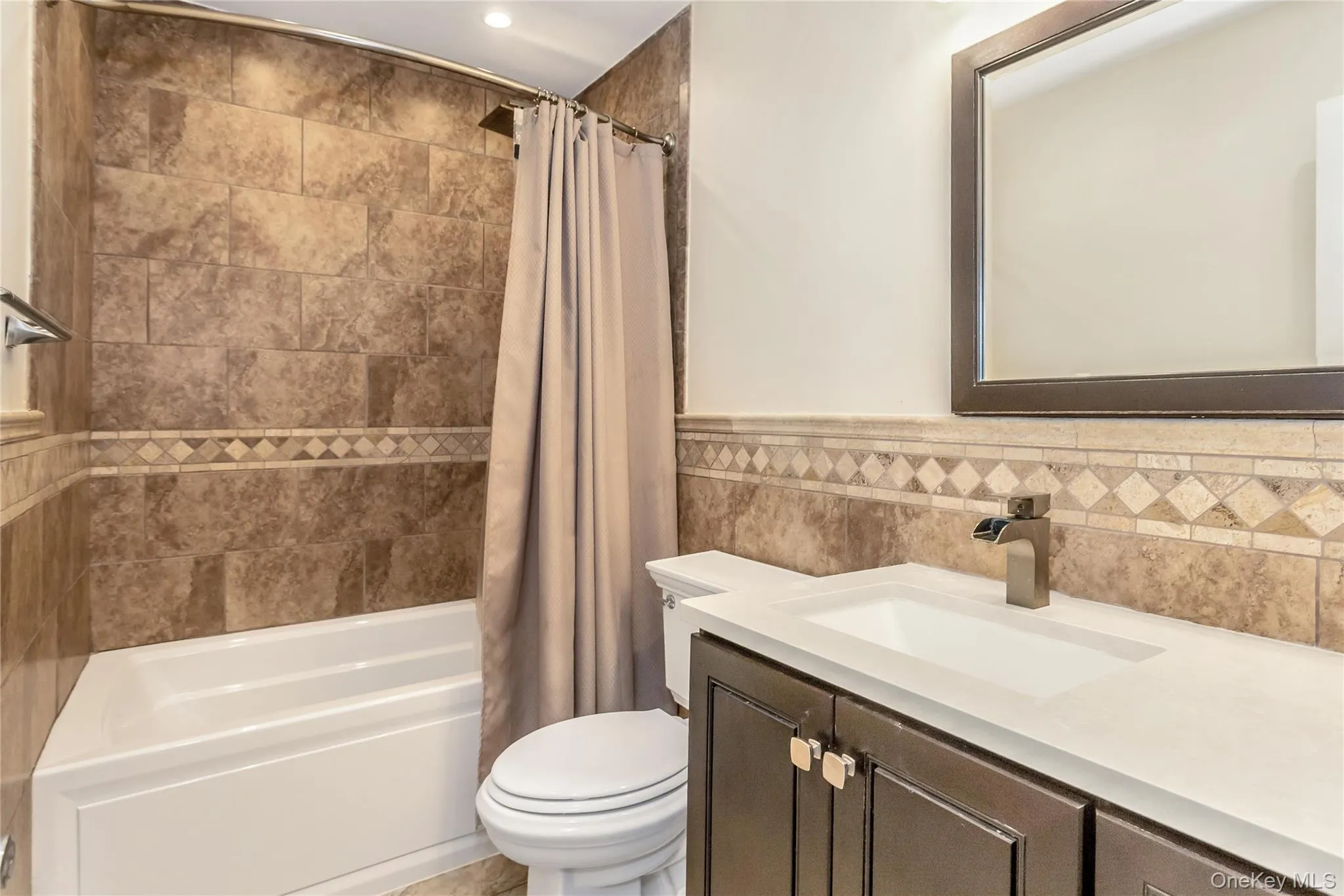 Bathroom featuring vanity, shower / tub combo with curtain, and tile walls Bathroom featuring vanity, shower / tub combo with curtain, and tile walls