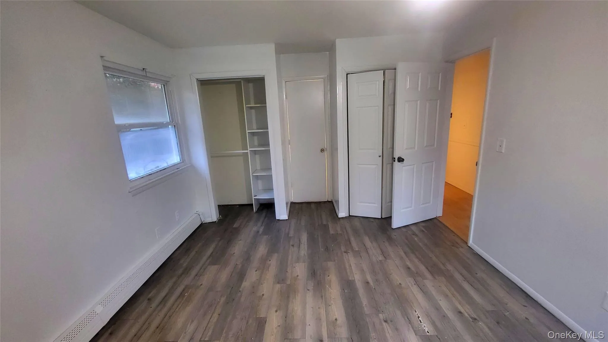 Unfurnished bedroom featuring baseboard heating, dark wood-type flooring, and a closet Unfurnished bedroom featuring baseboard heating, dark wood-type flooring, and a closet