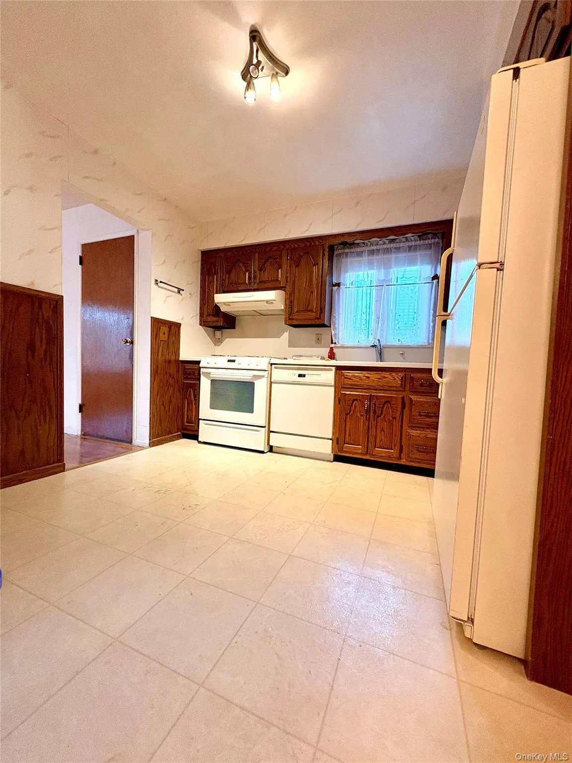 Kitchen featuring white appliances, light countertops, under cabinet range hood, brown cabinets, and wainscoting Kitchen featuring white appliances, light countertops, under cabinet range hood, brown cabinets, and wainscoting