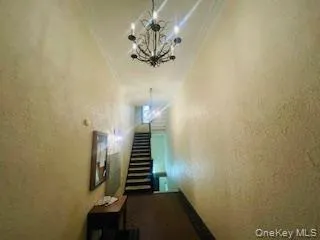 Hall with a textured wall, ornamental molding, stairs, and a chandelier Hall with a textured wall, ornamental molding, stairs, and a chandelier