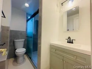 Full bathroom with vanity, a stall shower, tile walls, tile patterned floors, and recessed lighting Full bathroom with vanity, a stall shower, tile walls, tile patterned floors, and recessed lighting