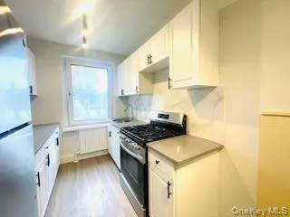 Kitchen featuring stainless steel gas range oven, white cabinetry, freestanding refrigerator, light countertops, and light wood-style floors Kitchen featuring stainless steel gas range oven, white cabinetry, freestanding refrigerator, light countertops, and light wood-style floors