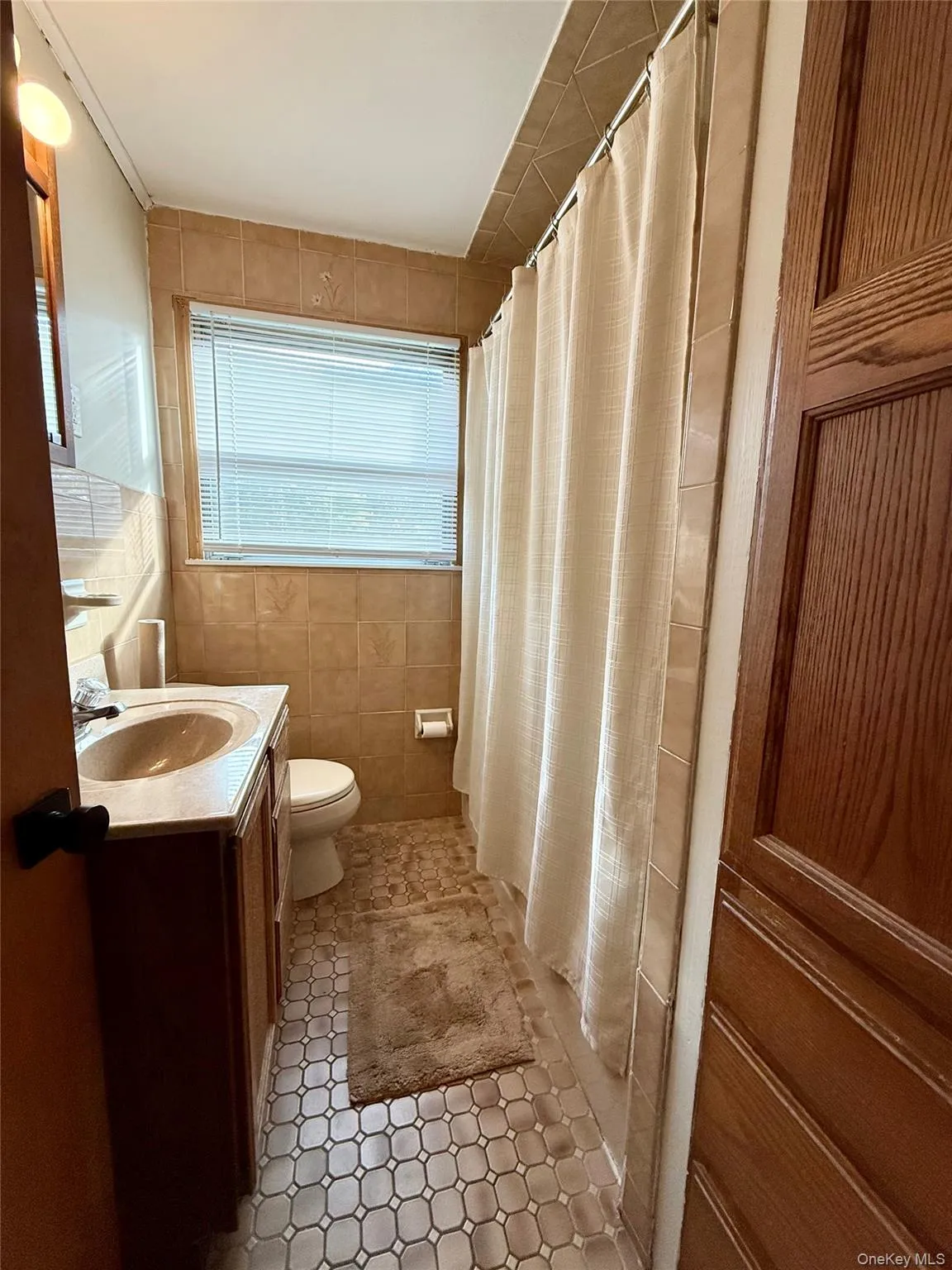 Full bath with tile walls, curtained shower, vanity, and light tile patterned flooring Full bath with tile walls, curtained shower, vanity, and light tile patterned flooring
