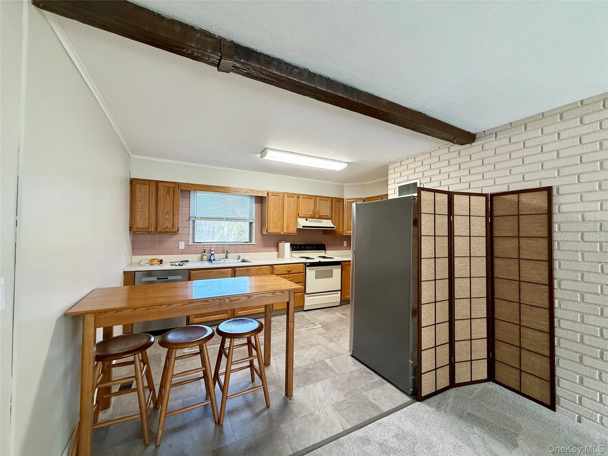 Kitchen featuring light countertops, freestanding refrigerator, electric range, brown cabinets, and beamed ceiling Kitchen featuring light countertops, freestanding refrigerator, electric range, brown cabinets, and beamed ceiling