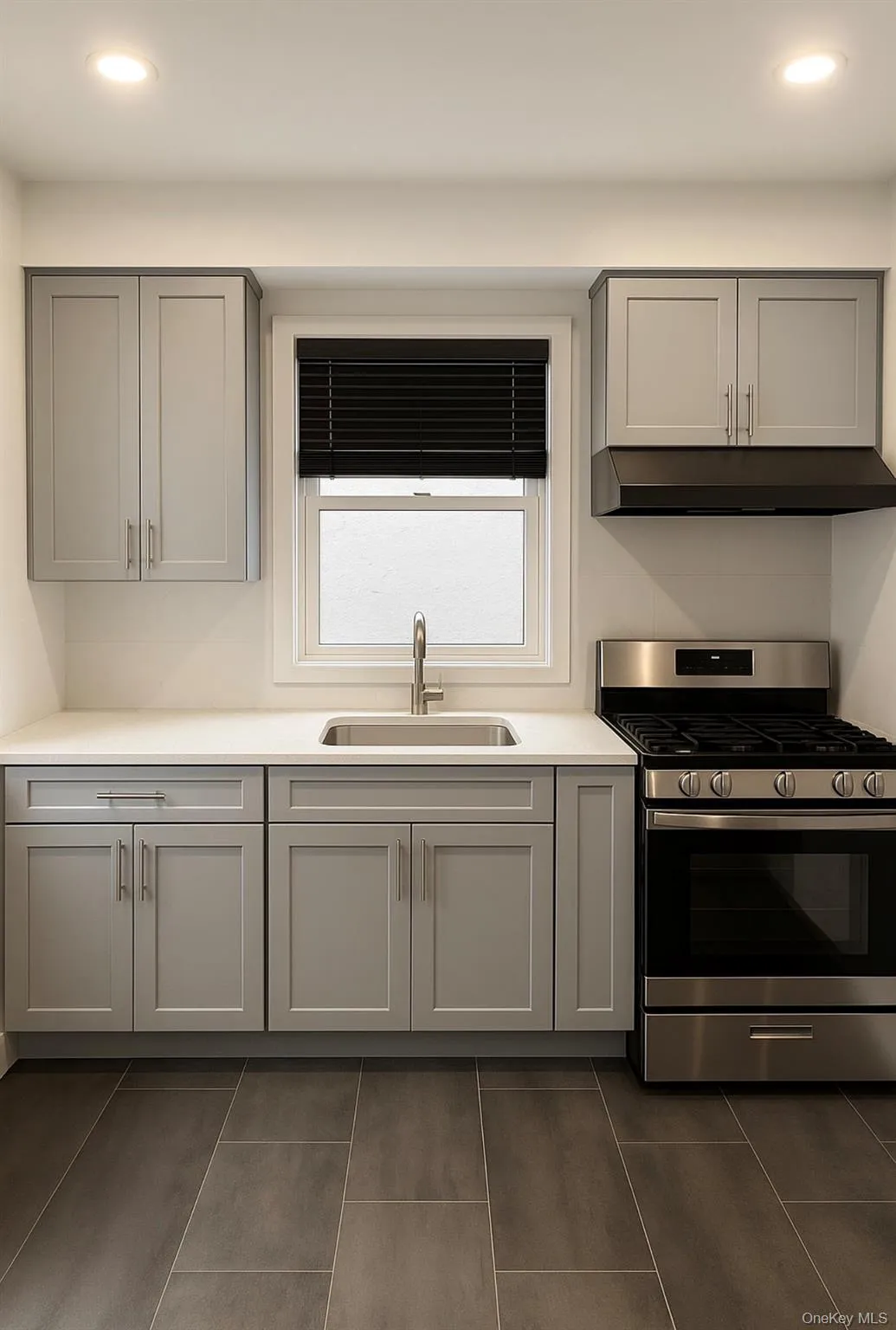 Kitchen with gray cabinets, recessed lighting, gas stove, under cabinet range hood, and dark tile patterned floors Kitchen with gray cabinets, recessed lighting, gas stove, under cabinet range hood, and dark tile patterned floors