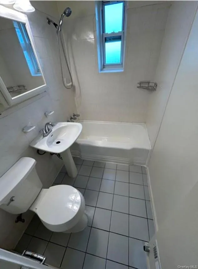 Full bathroom featuring sink, tiled shower / bath combo, tile patterned floors, toilet, and tile walls Full bathroom featuring sink, tiled shower / bath combo, tile patterned floors, toilet, and tile walls