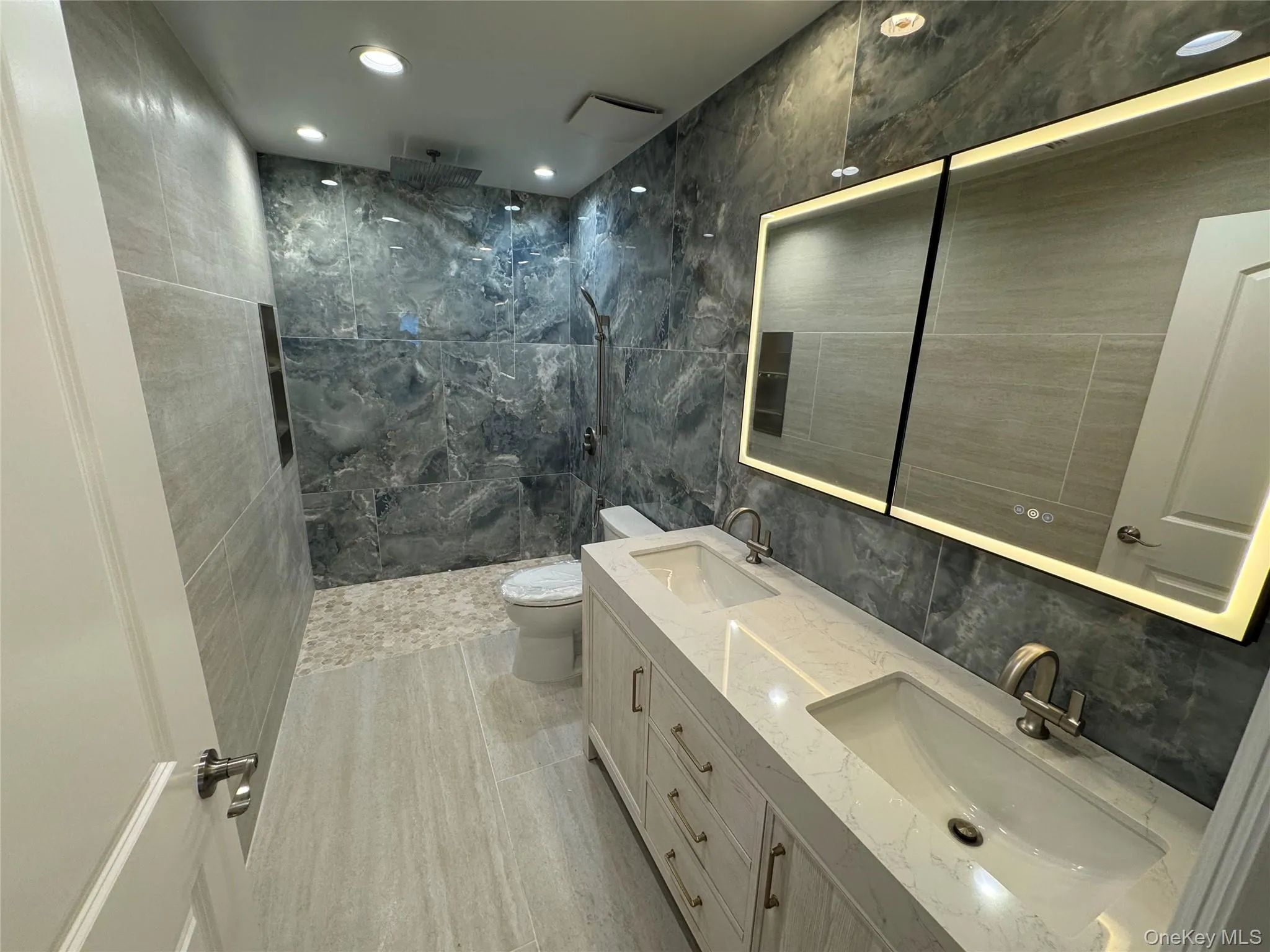 Full bath featuring tile walls, double vanity, a marble finish shower, and recessed lighting Full bath featuring tile walls, double vanity, a marble finish shower, and recessed lighting