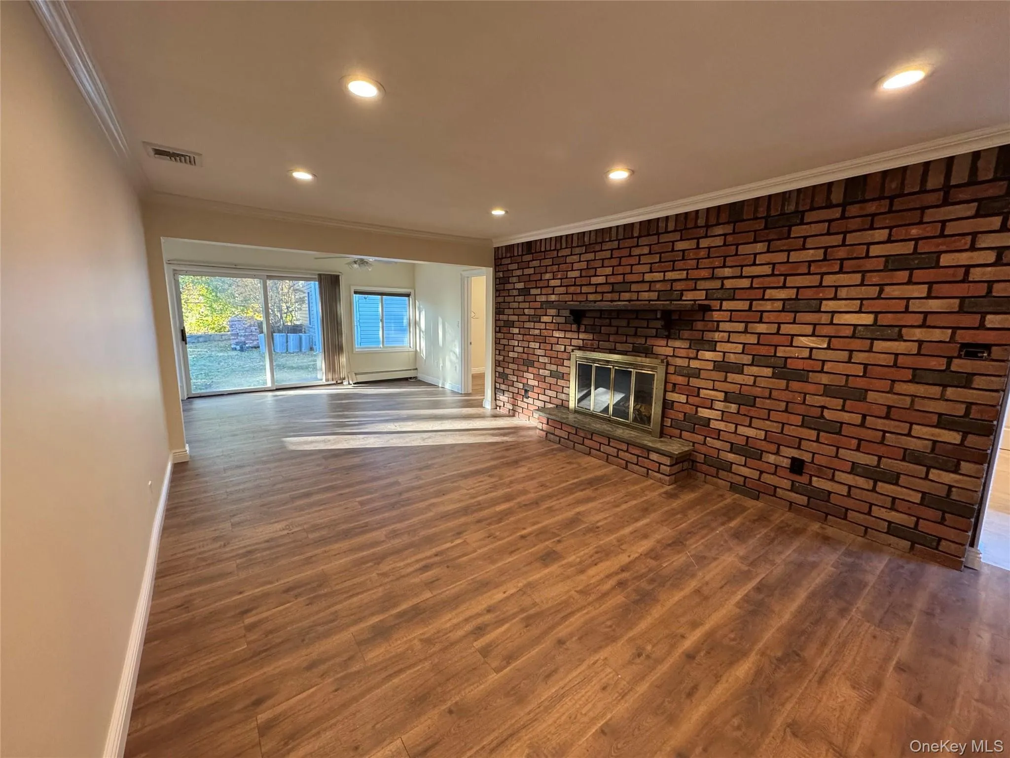 Unfurnished living room with brick wall, crown molding, dark wood-type flooring, a brick fireplace, and recessed lighting Unfurnished living room with brick wall, crown molding, dark wood-type flooring, a brick fireplace, and recessed lighting