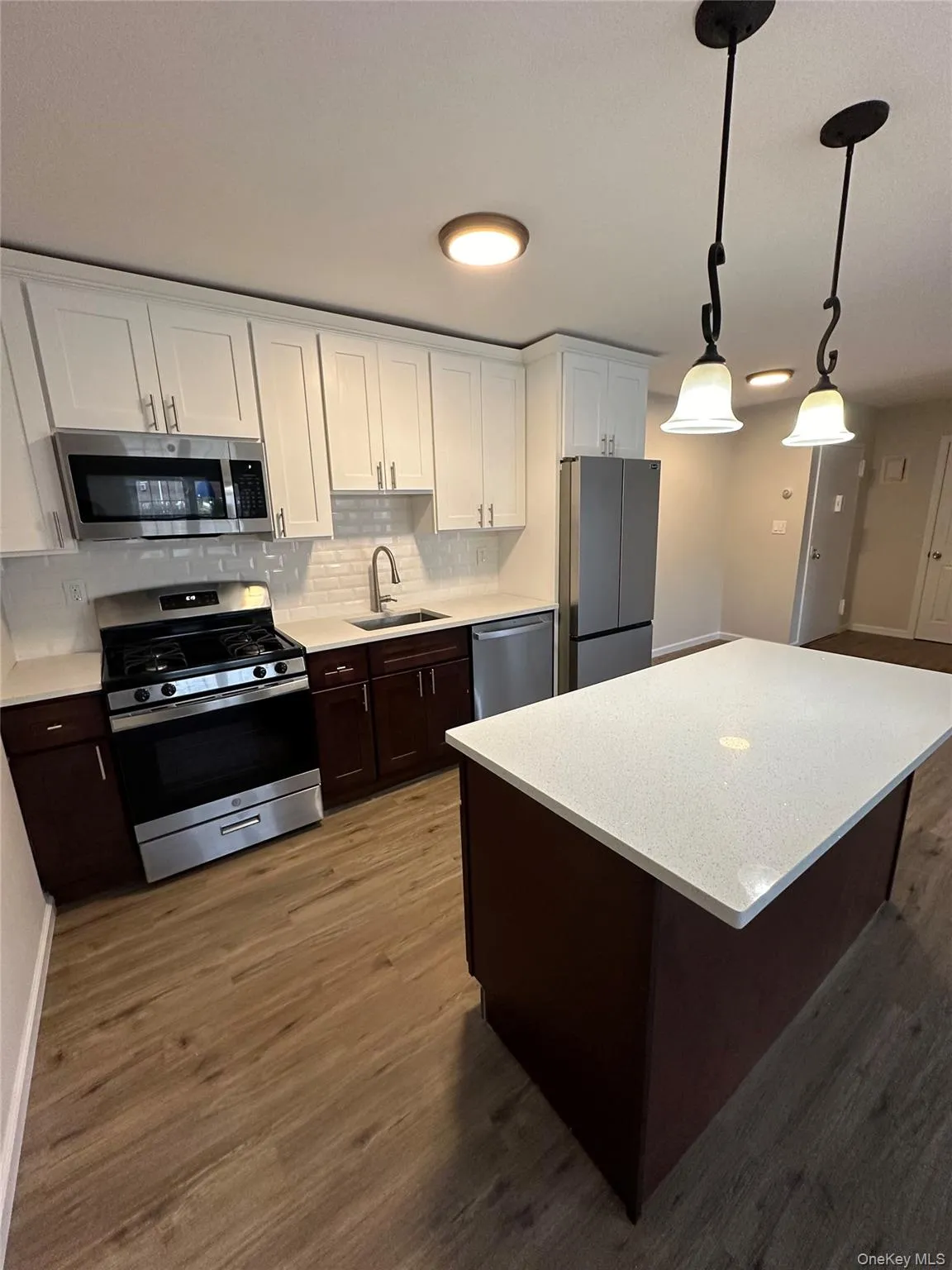 Kitchen featuring dark brown cabinetry, white cabinetry, appliances with stainless steel finishes, decorative backsplash, and dark wood-type flooring Kitchen featuring dark brown cabinetry, white cabinetry, appliances with stainless steel finishes, decorative backsplash, and dark wood-type flooring