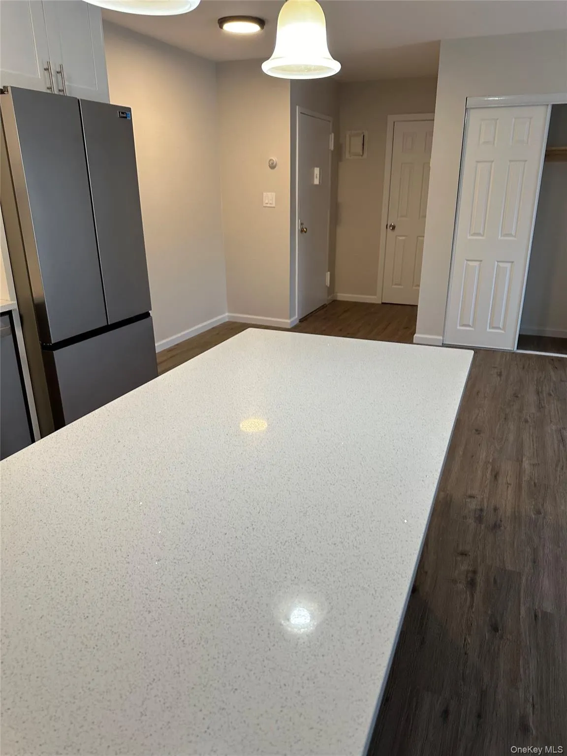 Kitchen featuring freestanding refrigerator, white cabinets, dark wood-style flooring, and light stone counters Kitchen featuring freestanding refrigerator, white cabinets, dark wood-style flooring, and light stone counters