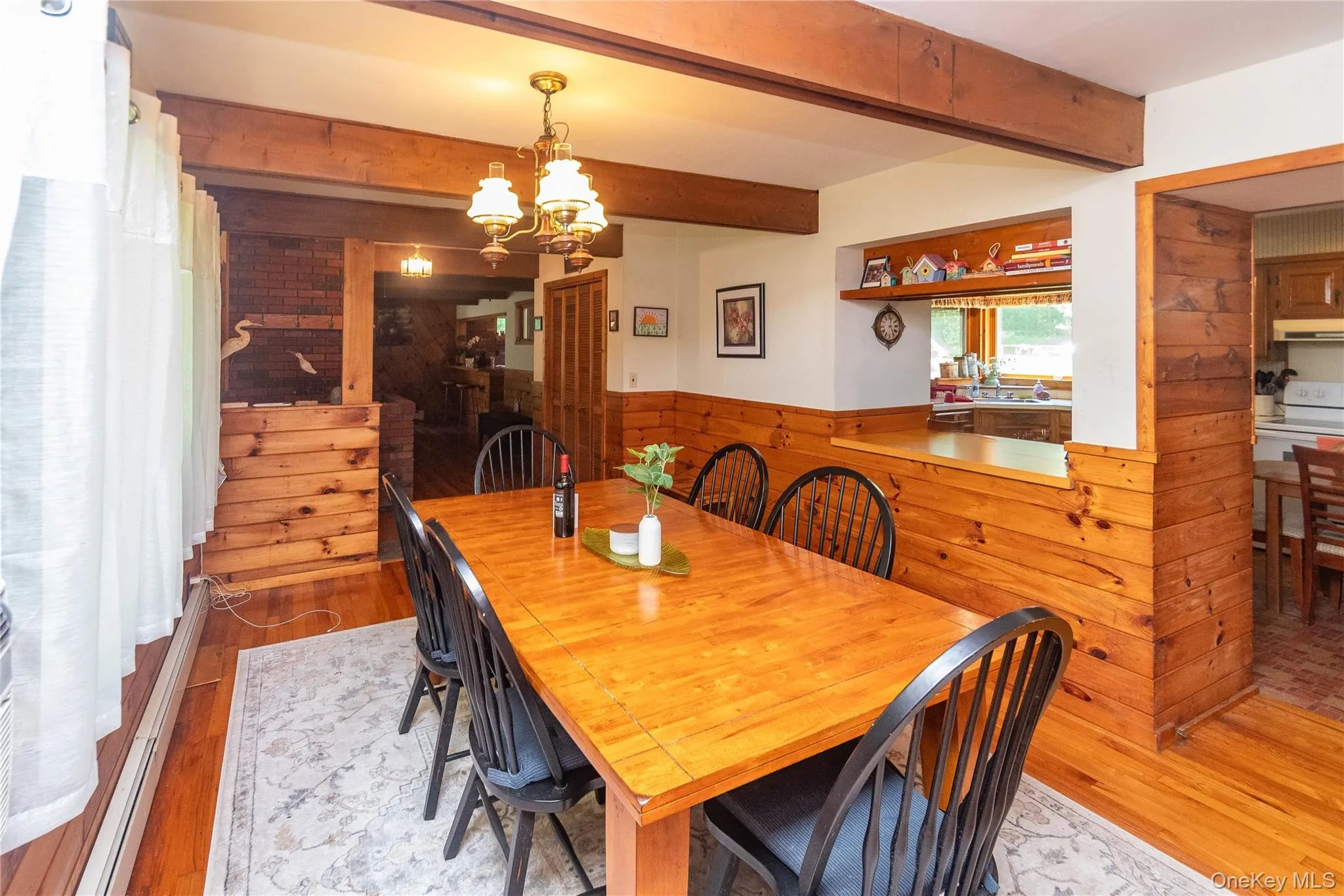 Dining room featuring wooden walls, light wood finished floors, a chandelier, a baseboard radiator, and wainscoting Dining room featuring wooden walls, light wood finished floors, a chandelier, a baseboard radiator, and wainscoting
