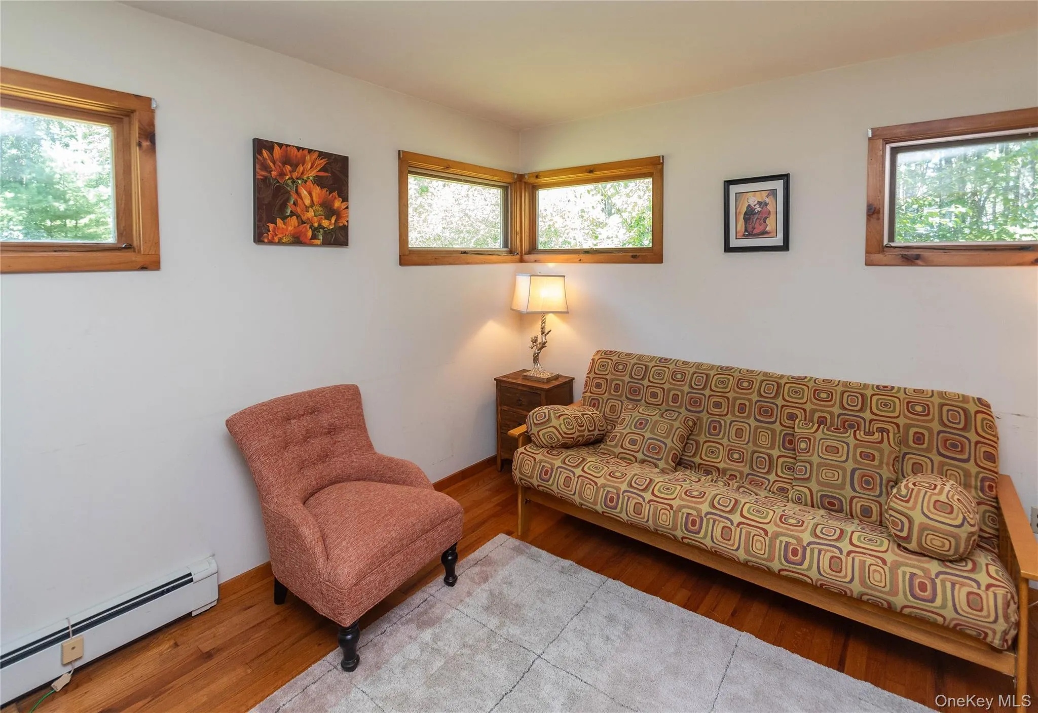 Living area featuring baseboard heating, healthy amount of natural light, and wood finished floors Living area featuring baseboard heating, healthy amount of natural light, and wood finished floors